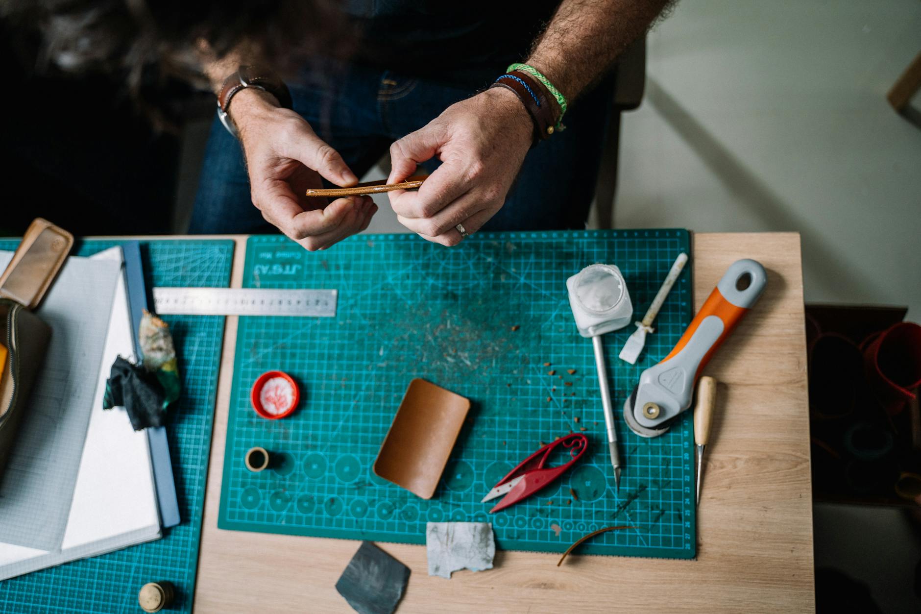 Close-up of skilled hands working leather on a workbench, surrounded by tools.
